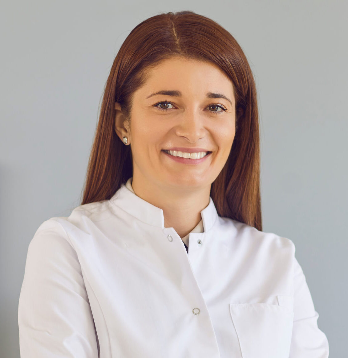 Happy positive woman in lab coat standing arms folded looking at camera. Portrait of reliable medical professional at work. Profile picture of young doctor, smiling hospital staff or online consultant