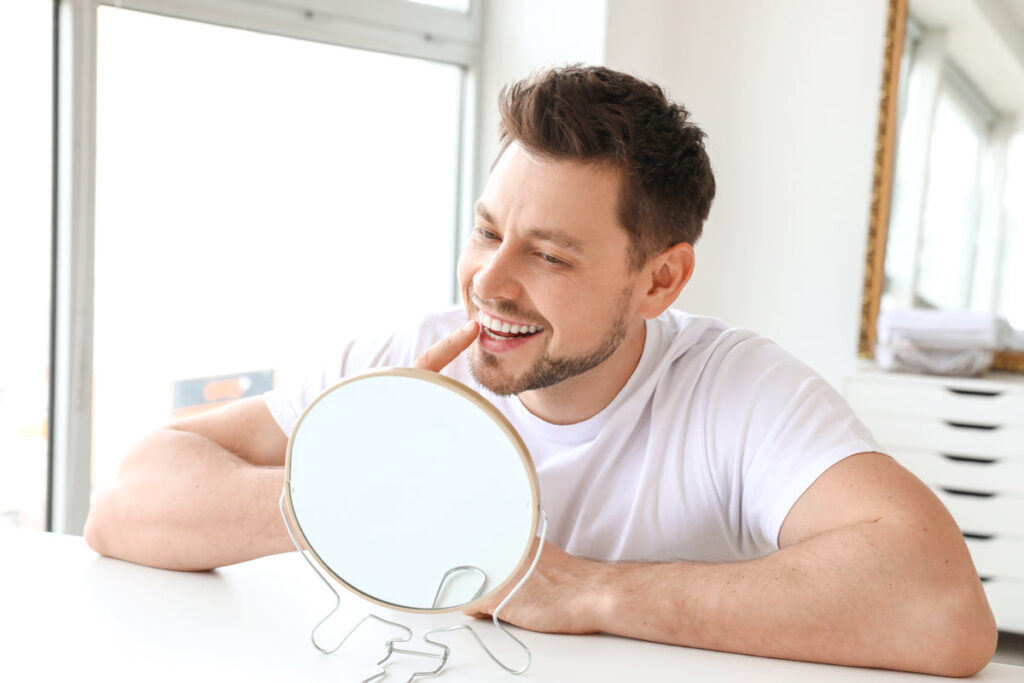 Man with healthy teeth looking in mirror at home